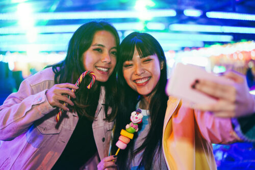 Happy asian girls having fun doing selfie outdoors at amusement park - Focus on right girl face